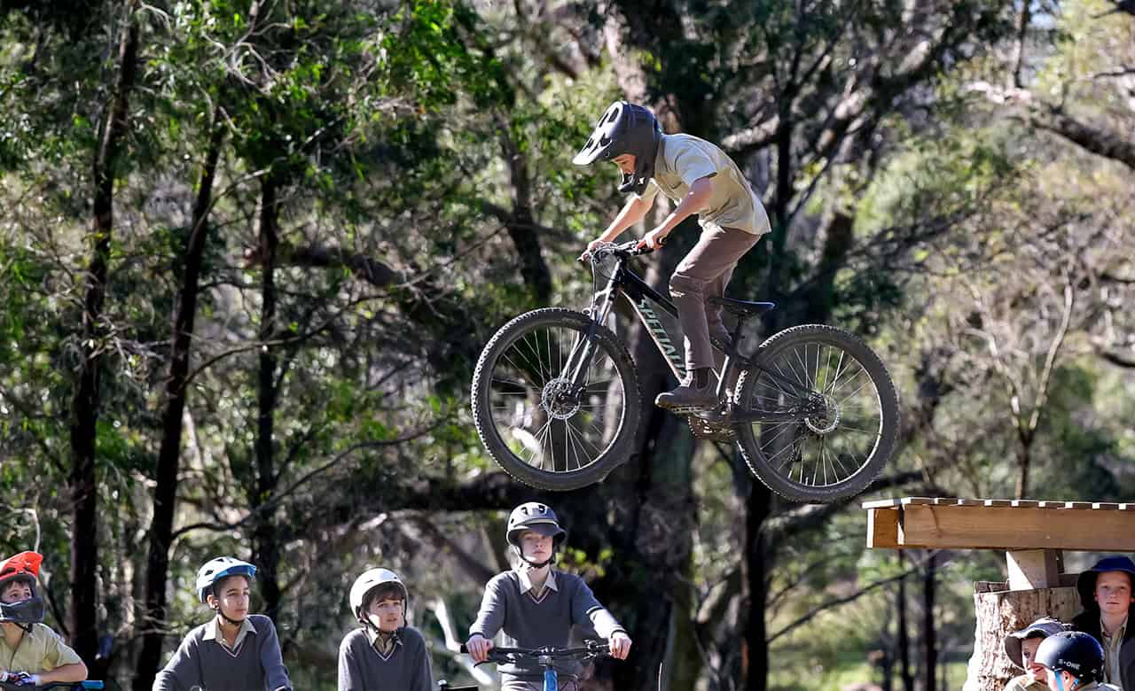 Tudor House student in his uniform riding his bike off a ramp