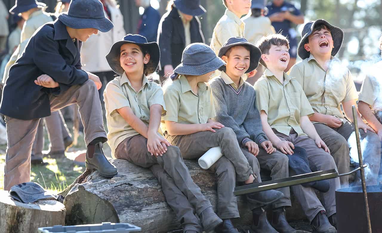 A group of Tudor House students in their uniforms sitting near a campfire laughing