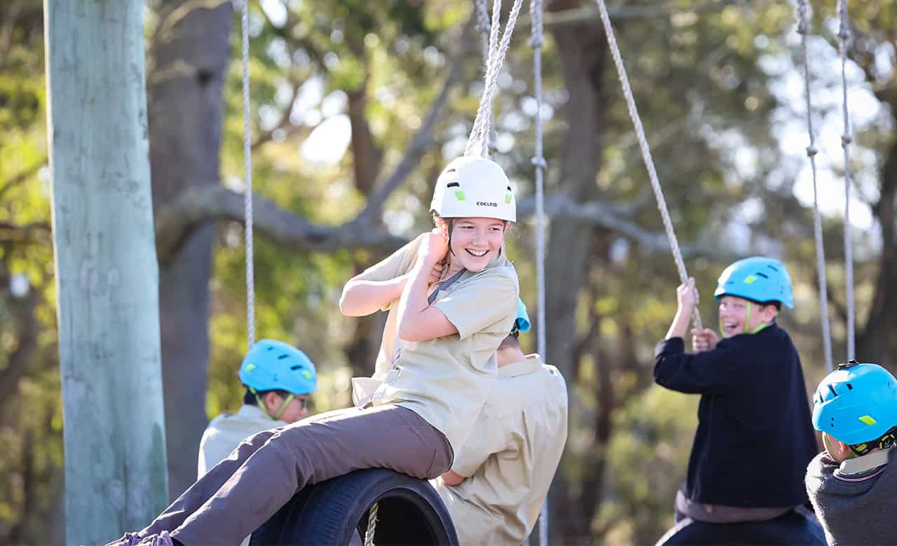 A happy Tudor House student in her uniform on a tire swing at the Low Ropes course