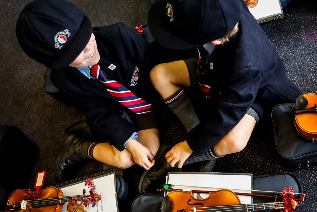 Tudor House students sitting on the floor with their violins as they wait to perform